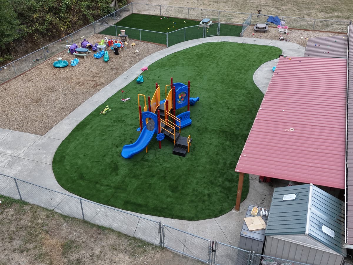 Aerial view of the new turf playground at Fort Nugent, with the play structure, the bark play area with ride-on toys and the second fenced yard