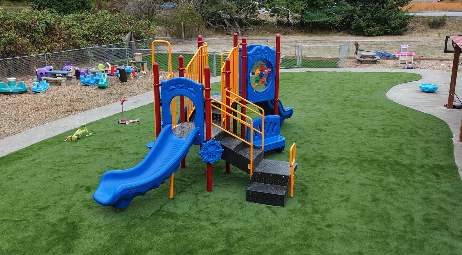 The new turf playground at our Fort Nugent location, with a blue and yellow play structure and slide on bright green artificial turf