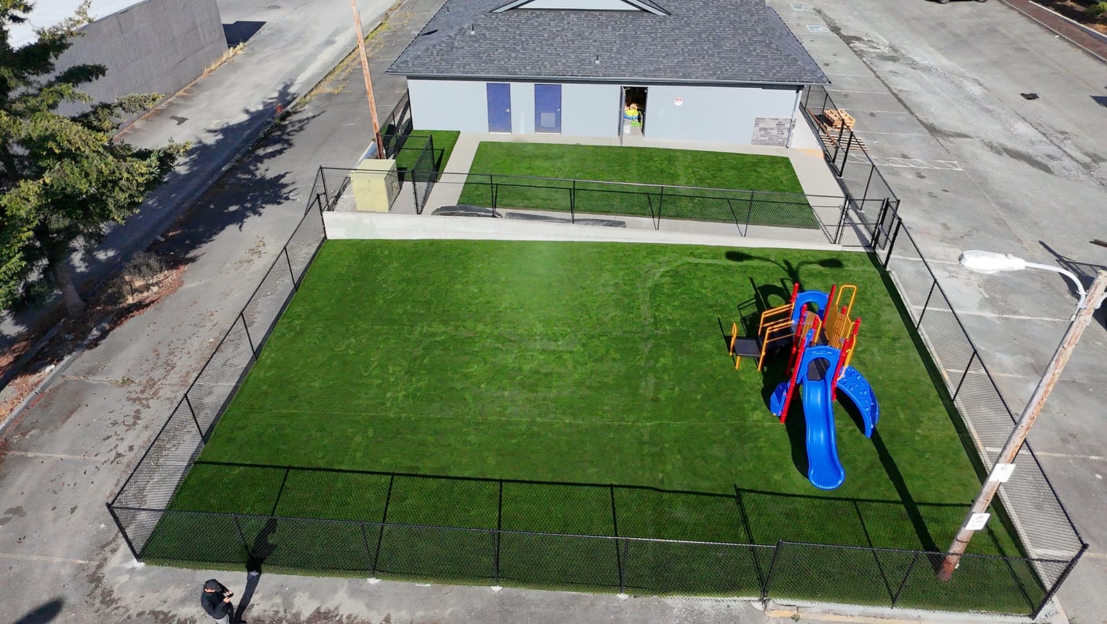 Aerial view of the fenced turf play yard and playground at the Midway Blvd location