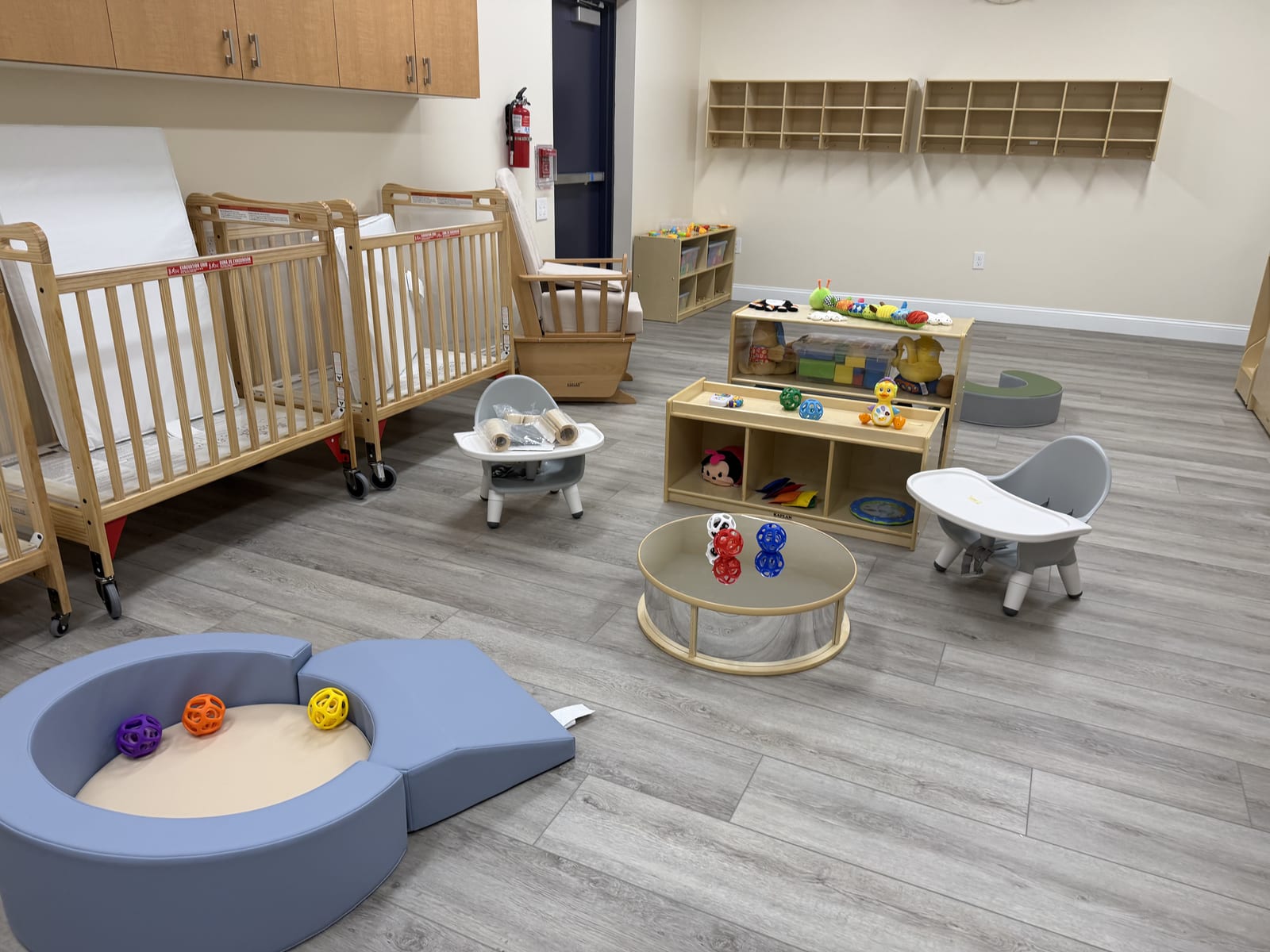 Infant room at the Midway Blvd location with cribs, a soft play pit, and high chairs