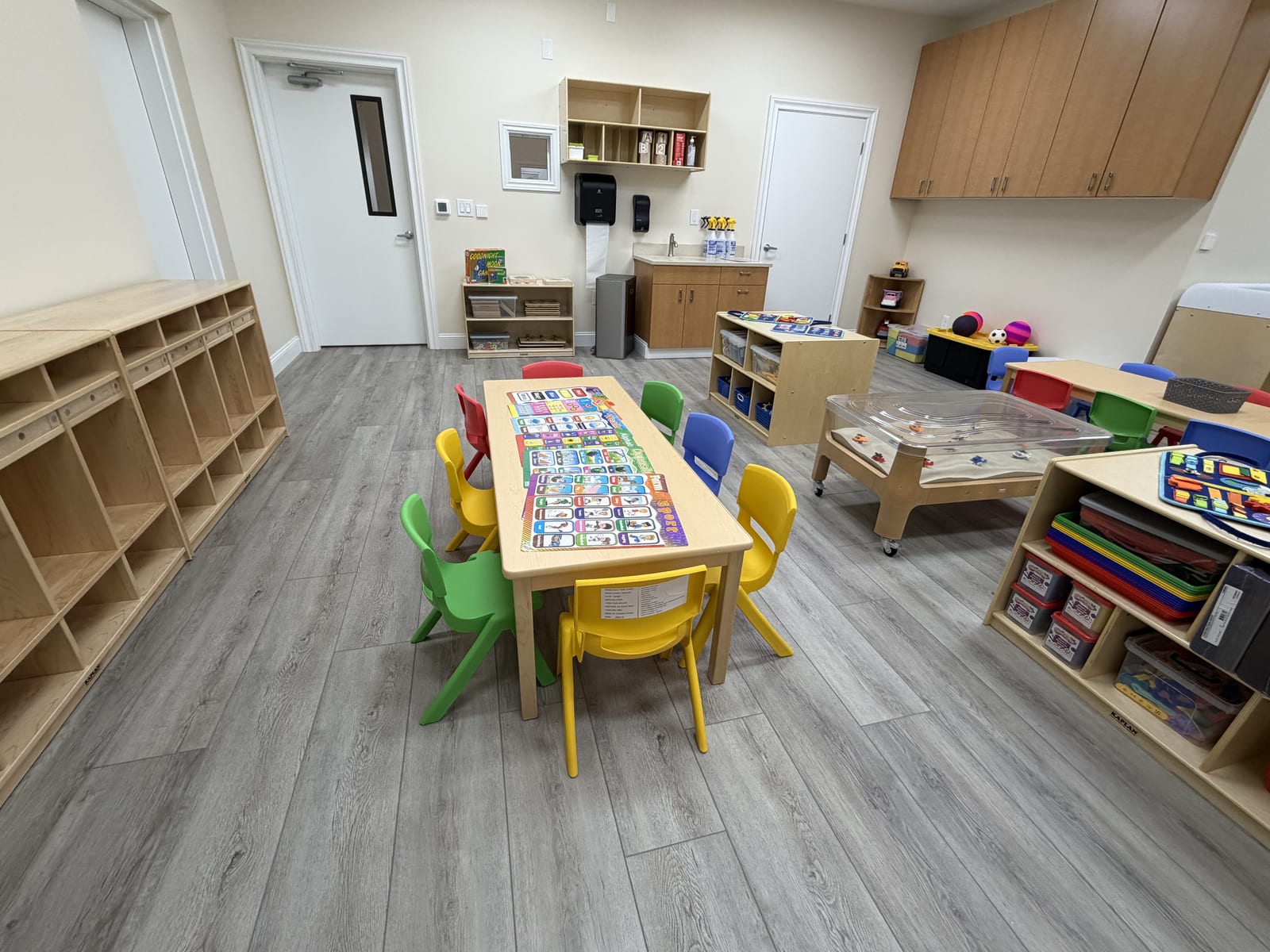 Preschool classroom with a learning table, colorful chairs, and a full wall of cubbies
