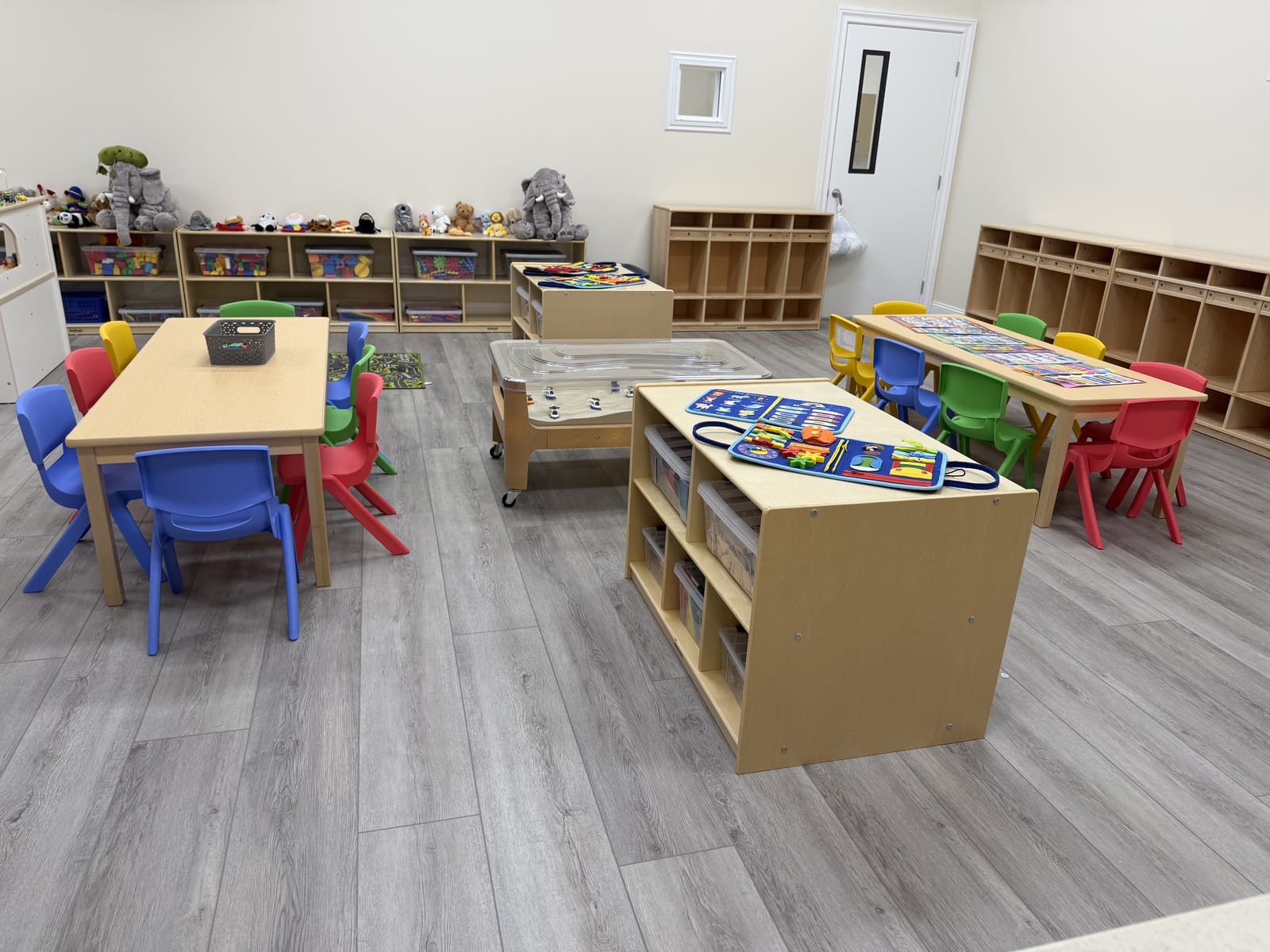 Toddler classroom with activity tables, colorful chairs, a sensory table, and open shelving